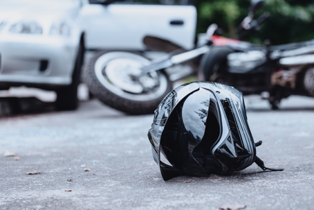 Close-up of a black biker helmet on the street with overturned motorbike in the background